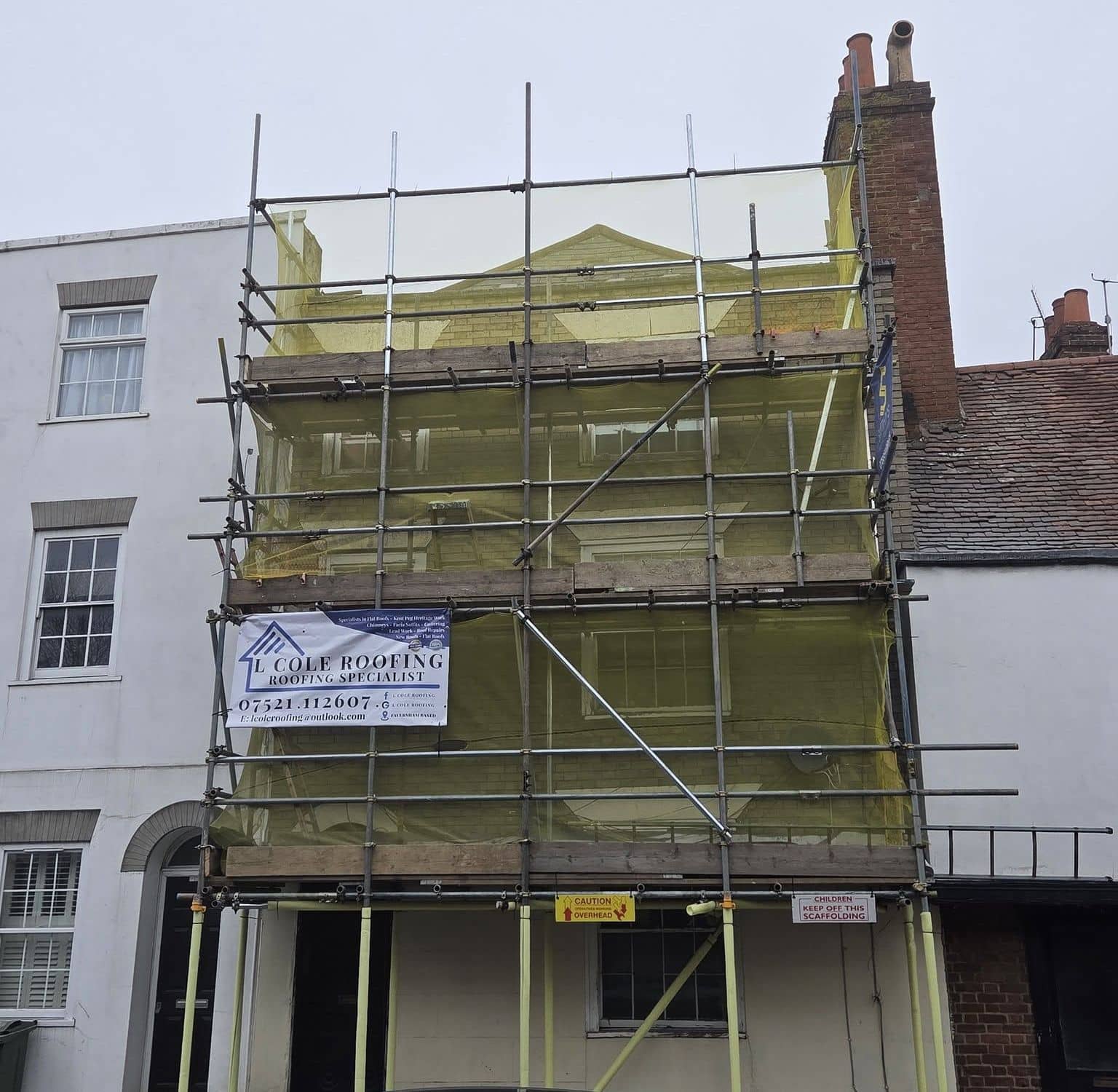 Scaffolding with an L Cole Roofing banner on a period town house